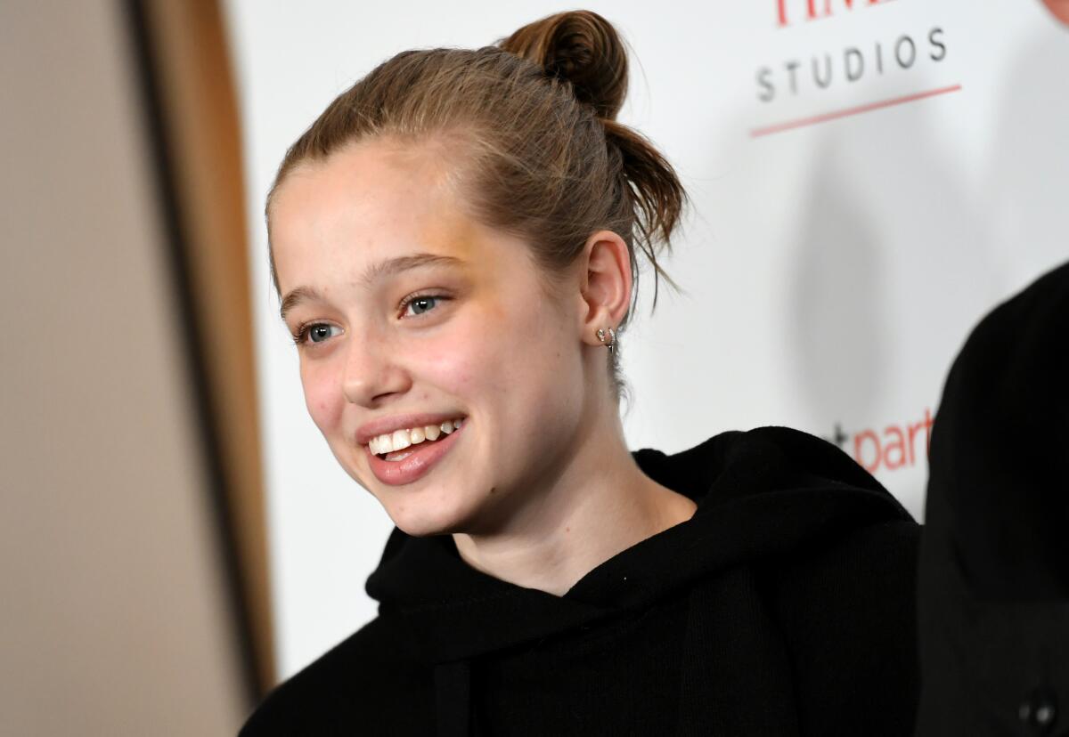 Shiloh Jolie-Pitt looking to the side and smiling in a black hoodie with her hair pinned up in a messy bun