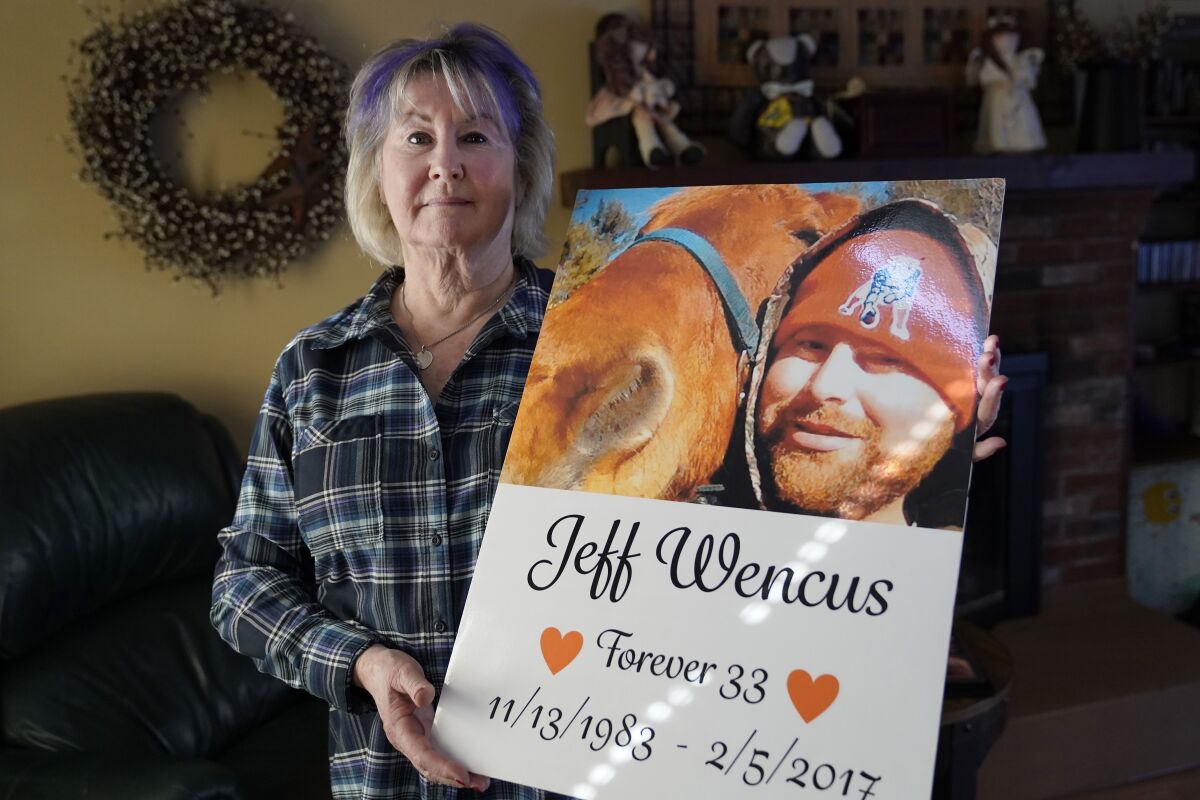 Lynn Wencus, of Wrentham, Mass., holds a poster, with a likeness of her son Jeff, at her home, in Wrentham, Wednesday, March 2, 2022. Wencus lost her son to a heroin overdose in 2017. OxyContin maker Purdue Pharma and virtually all U.S. states have agreed to a new settlement of opioid lawsuits. The deal reached Thursday, March 3, 2022, would require members of the Sackler family who own the drugmaker to pay $5.5 billion to $6 billion in cash. They also apologized. A bankruptcy judge must still approve the deal. (AP Photo/Steven Senne)