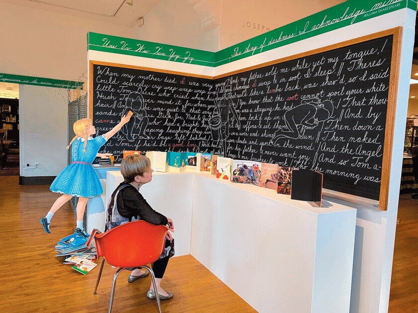 Artist Christine Oatman takes the teacher's seat in 'This Thing of Darkness,' where a girl standing on a toppling pile of Dr. Seuss books is erasing some of what's written on the blackboard - William Blake's poem 'The Chimney Sweeper,' with drawings of hardworking children superimposed.