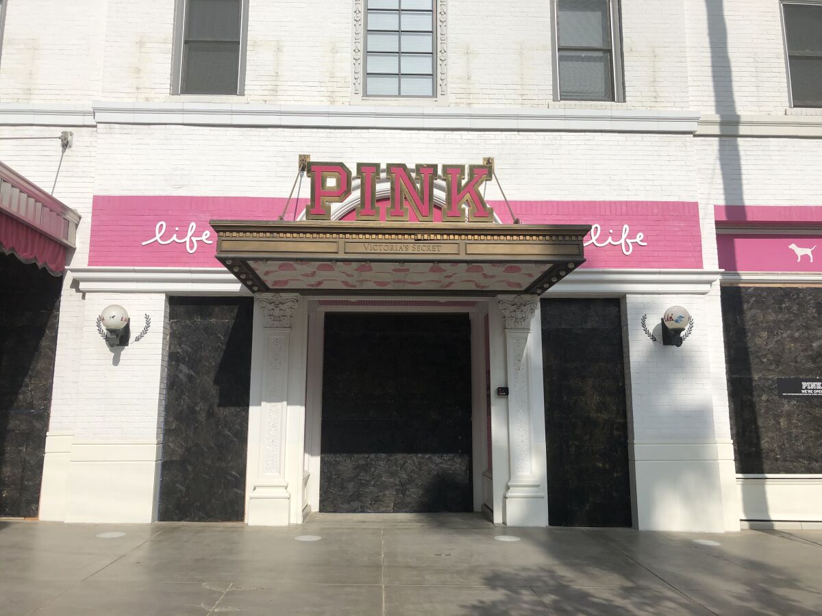 A white building with a sign that reads "Pink" is covered with plywood painted black.