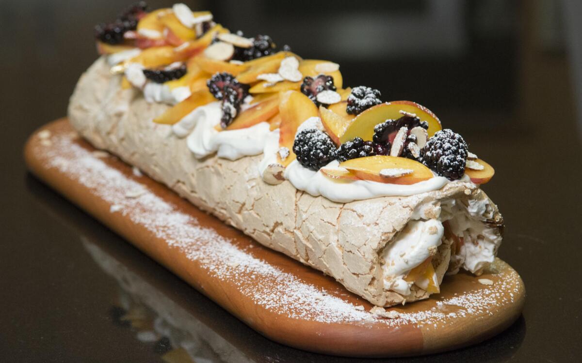 Rolled pavlova filled with whipped cream and fruit and topped with more cream, peaches, blackberries and sliced almonds.