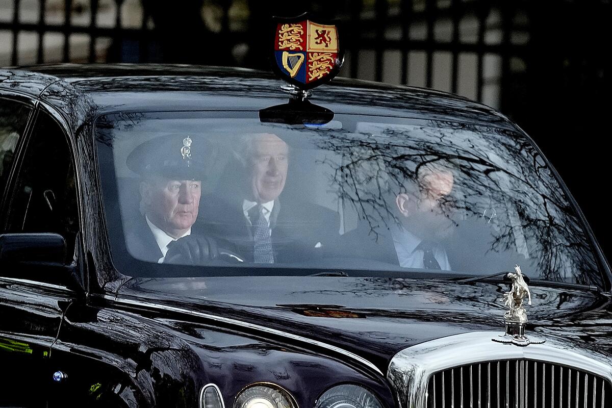 King Charles III with attendants behind windshield of royal car