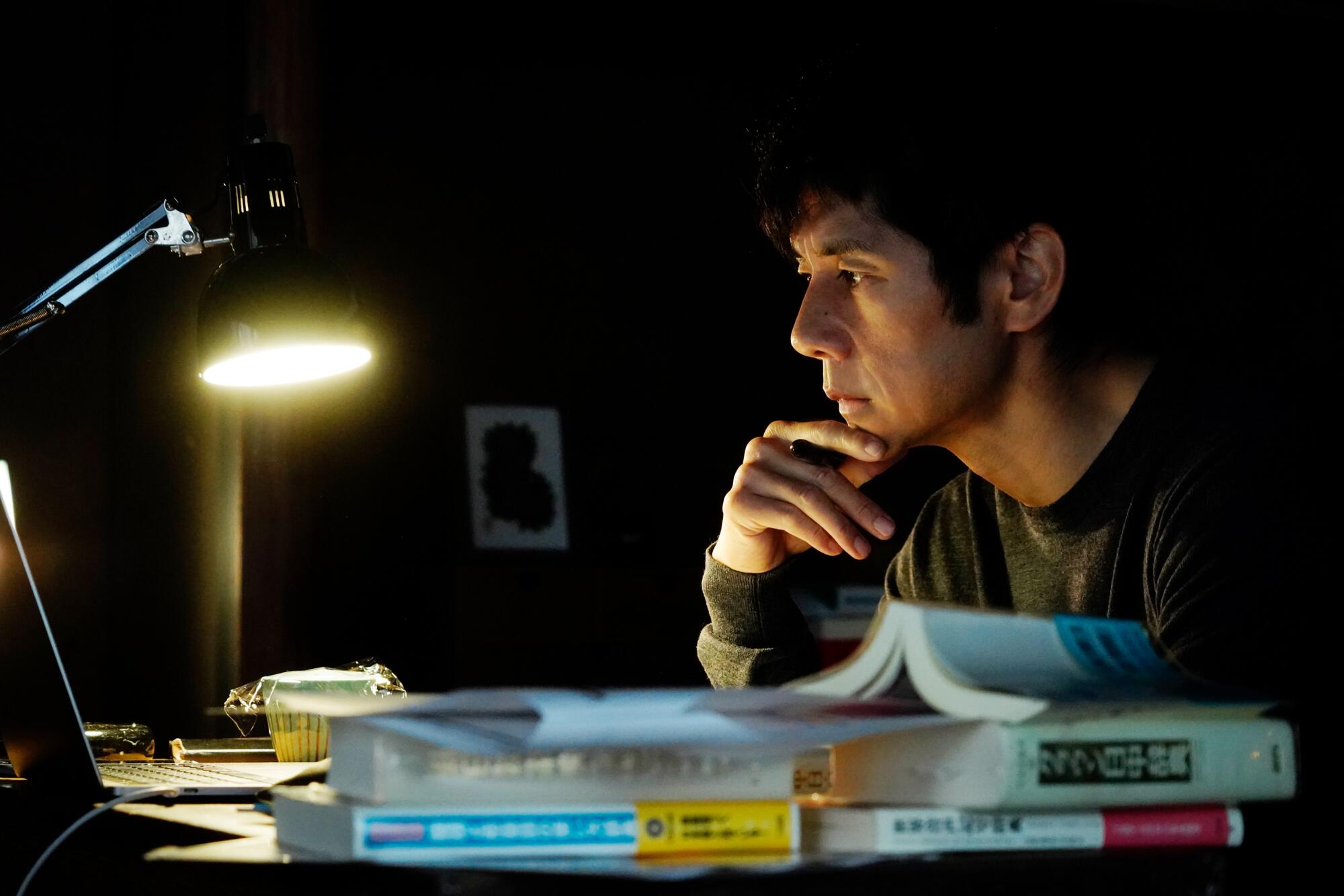 A man sits lost in thought at a desk in a scene from the film "Drive My Car."