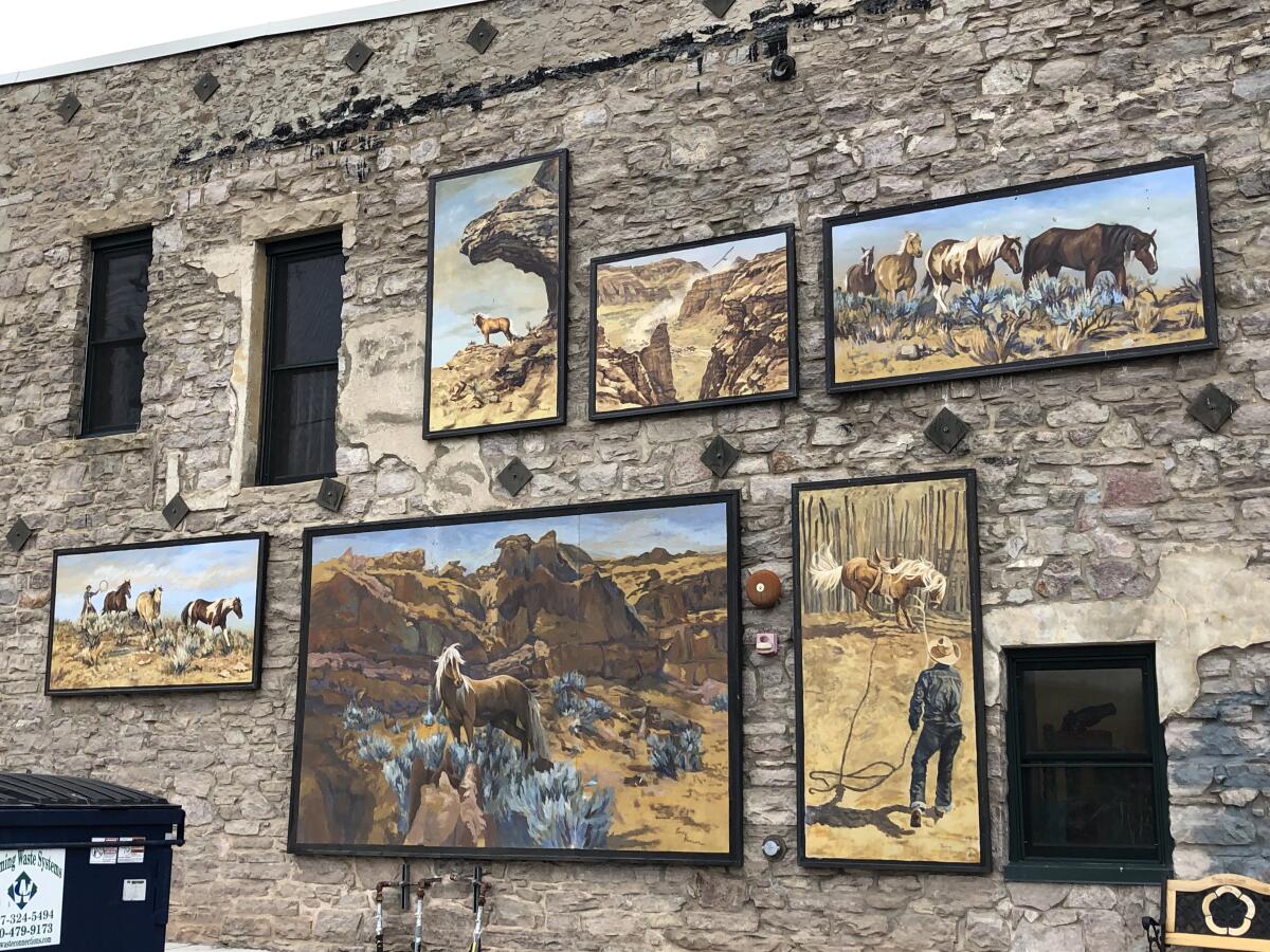 The side of a stone building with paintings of horses in a Western landscape.