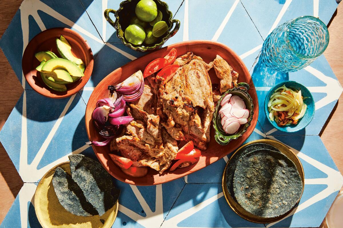 Poc chuc, marinated and grilled slices of pork shoulder, surrounded by tortillas and sliced vegetables.