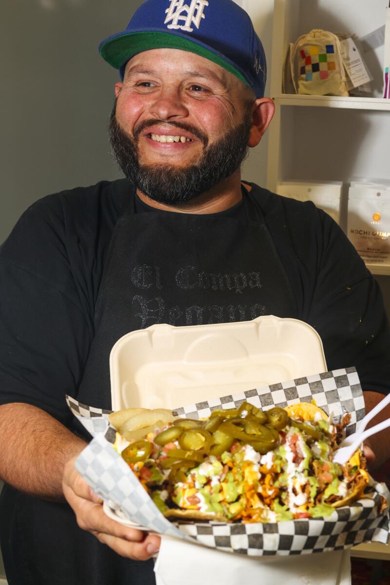 A portrait of a bearded man holding a takeout container of nachos.