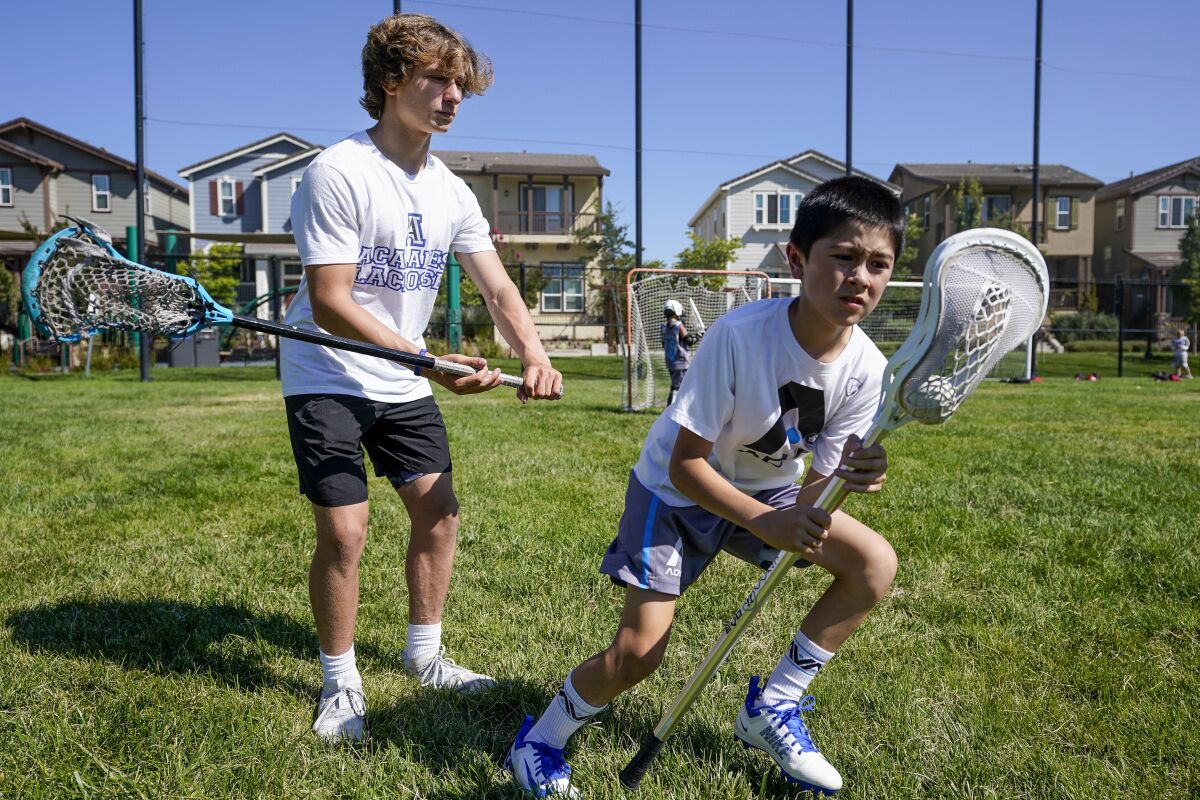 Zach Appel, right, Acalanes High School Varsity Lacrosse player, coaches 11-year-old Noah Shacklford on Tuesday, July 28, 2020 in Orinda, Calif. Zach and his friend Owen Estee have launched Lacrosse Against Hunger, to offer lacrosse coaching sessions to 7-14 year olds in exchange for a charitable donation to White Pony Express. All money raised goes directly to White Pony Express through Lacrosse Against Hunger's GoFundMe page. (AP Photo/Tony Avelar)