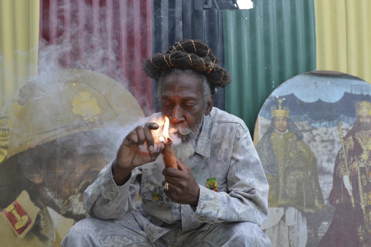 FILE - In this Aug. 28, 2014 file photo, legalization advocate and reggae legend Bunny Wailer smokes a pipe stuffed with marijuana during a "reasoning" session in a yard in Kingston, Jamaica. Wailer, a reggae luminary who was the last surviving member of the legendary group The Wailers, died on Tuesday, March 2, 2021, in his native Jamaica, according to his manager. He was 73. (AP Photo/David McFadden, File)