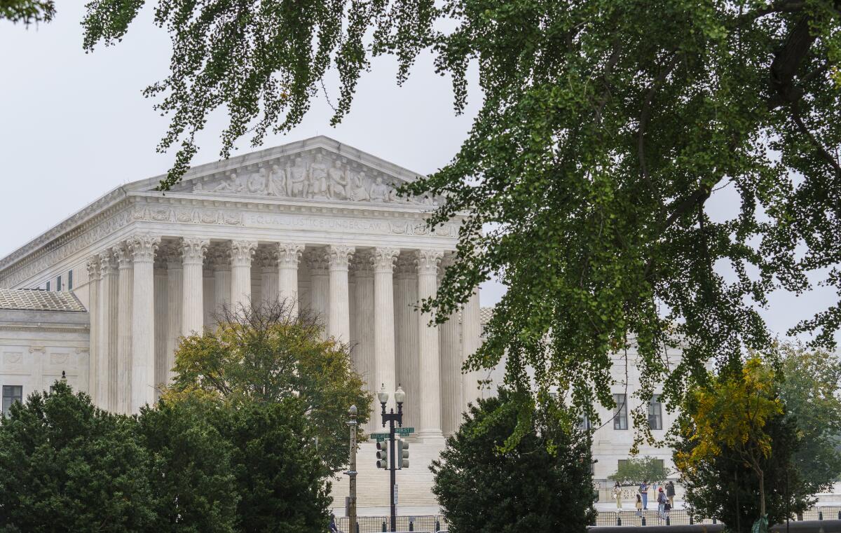 A view of the facade of the Supreme Court building with rows columns and steps. Trees are in the foreground.