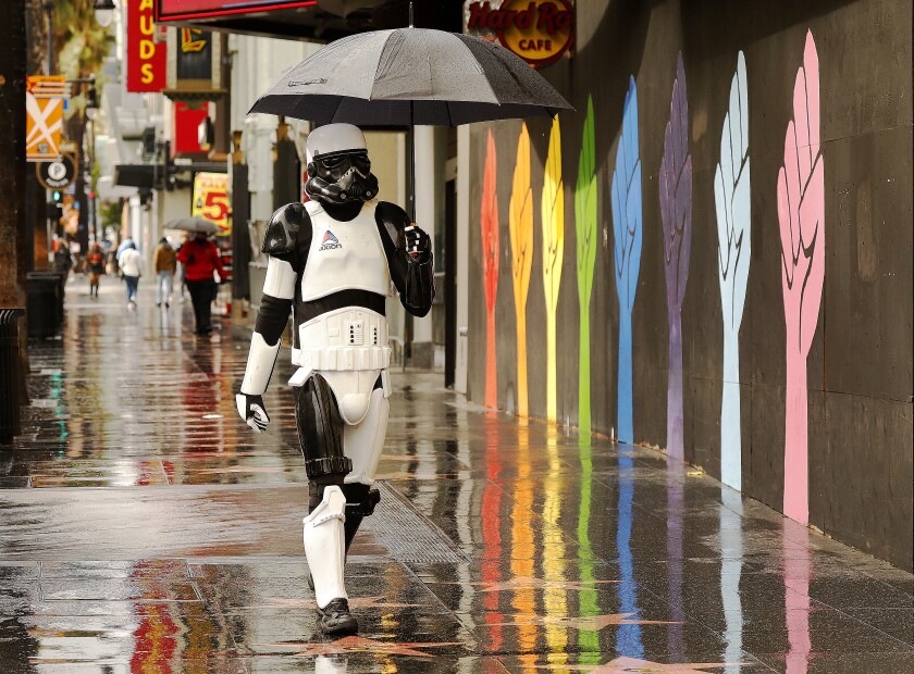 A person in a Star Wars stormtrooper costume walks under an umbrella on a wet sidewalk