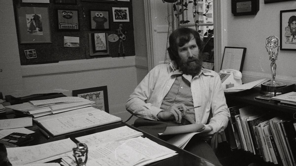 Jim Henson sitting at a desk holding a pencil and some paper.