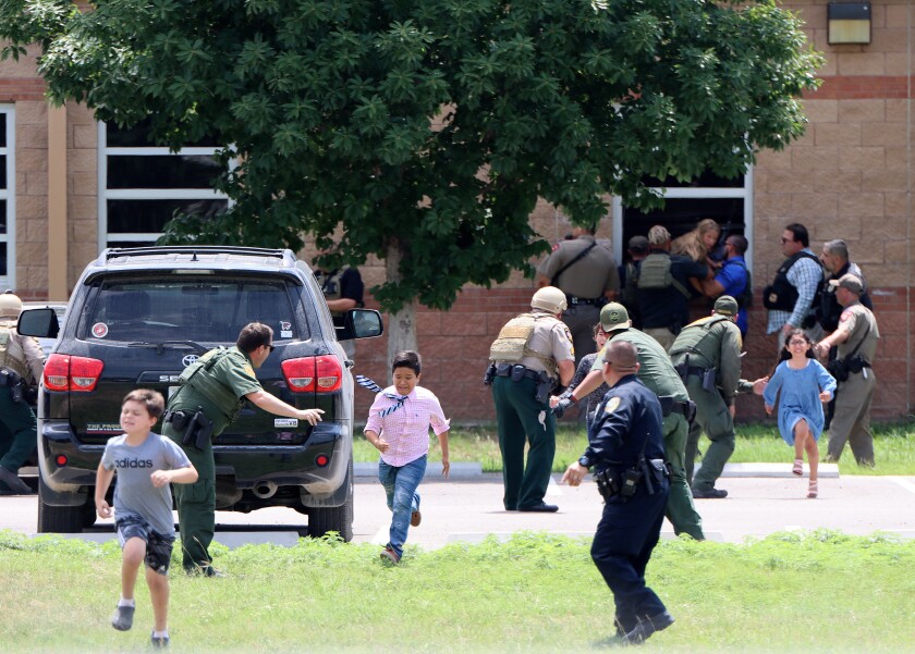 Children run from a school and police guide them.