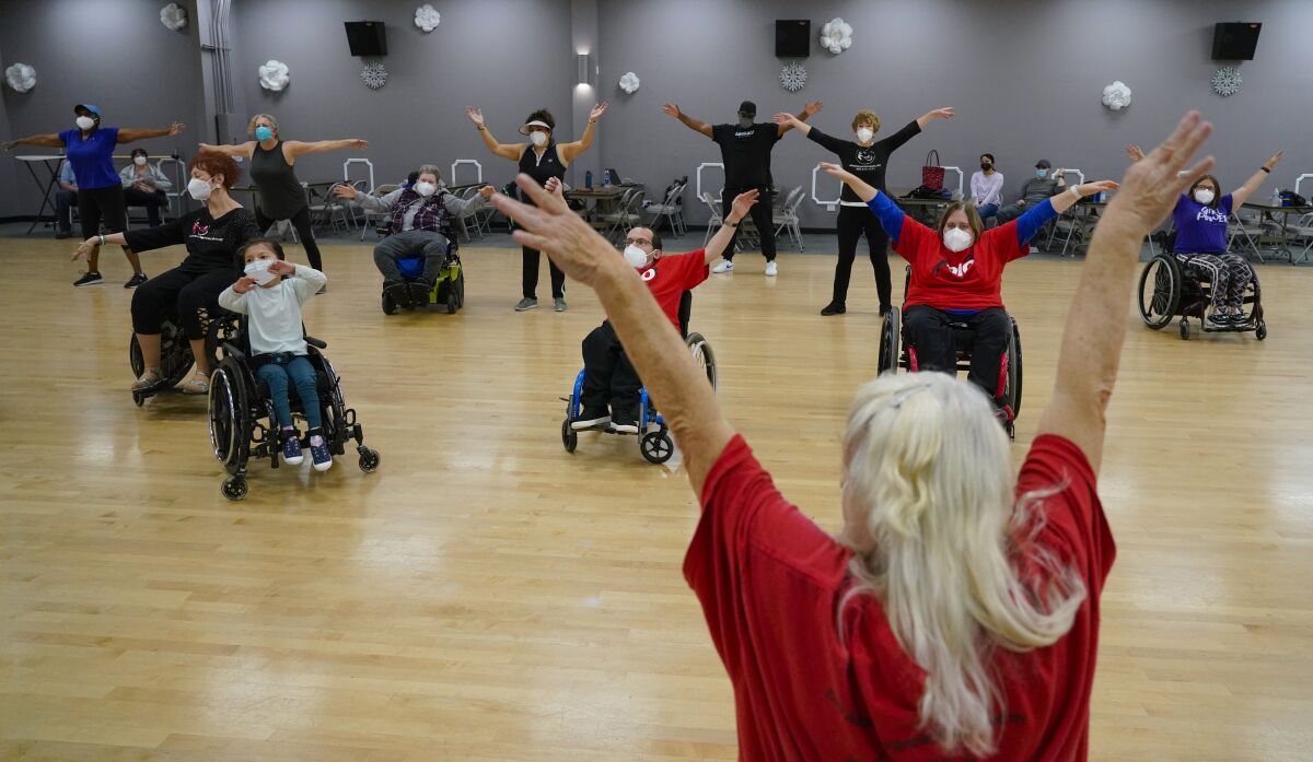 Dancers both sitting in wheelchairs and standing up stretch their arms out in a dance studio
