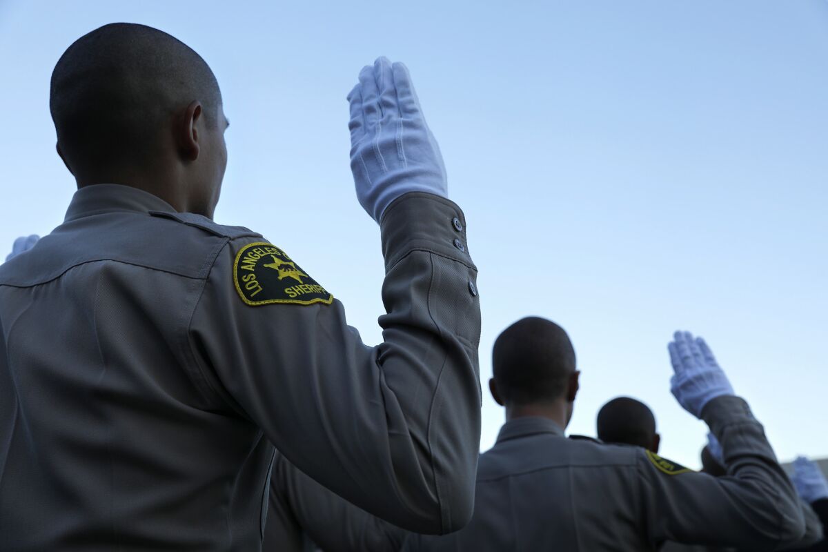 New Los Angeles County sheriff's deputies raise their right hands during the swearing-in portion of a graduation ceremony.