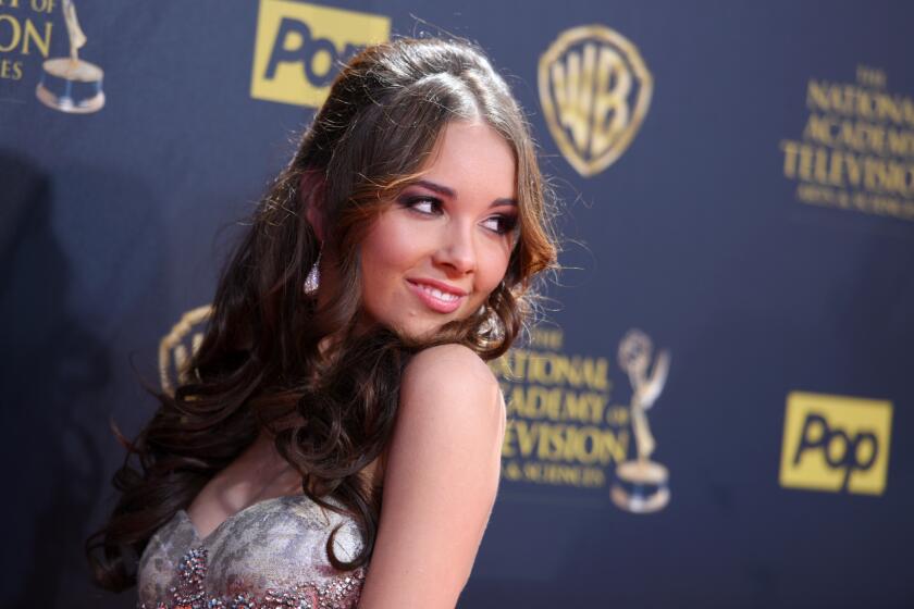 Haley Pullos poses over her shoulder in a gray patterned dress against a navy blue background.