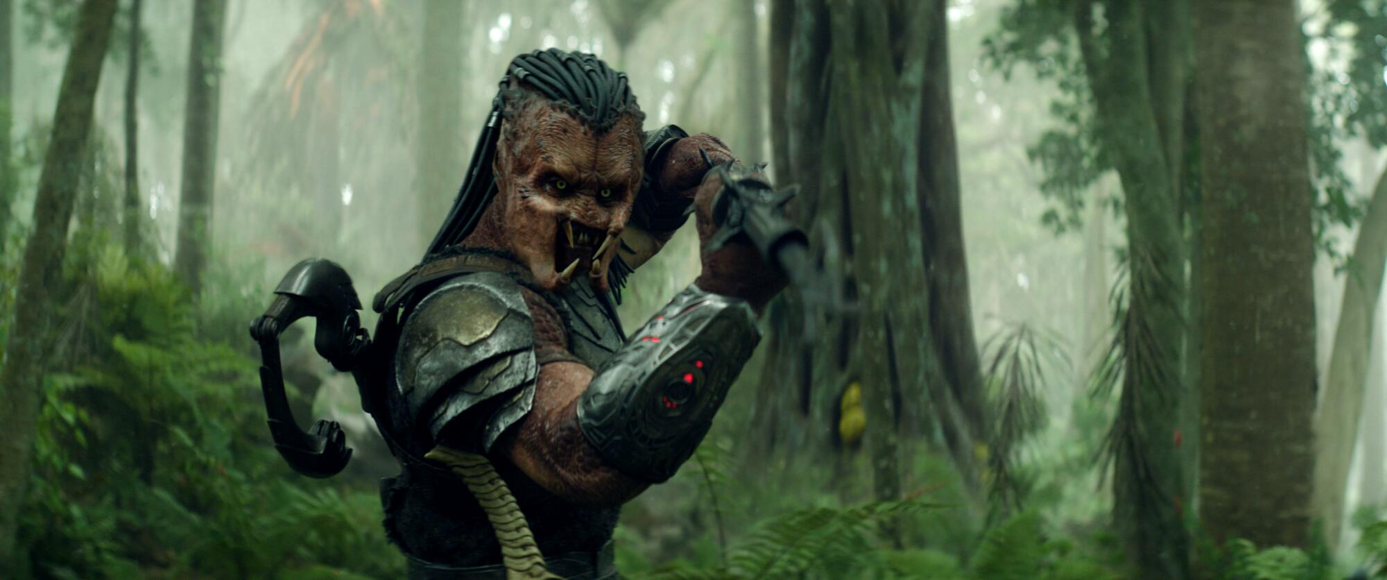 An alien warrior raises a weapon in a forest.