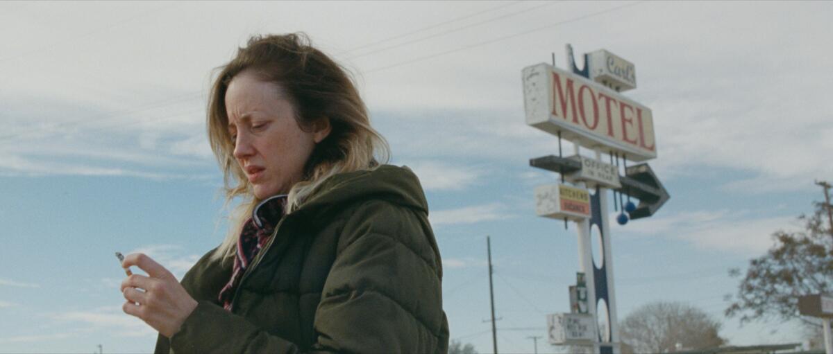 A woman holds a cigarette beneath a motel sign 