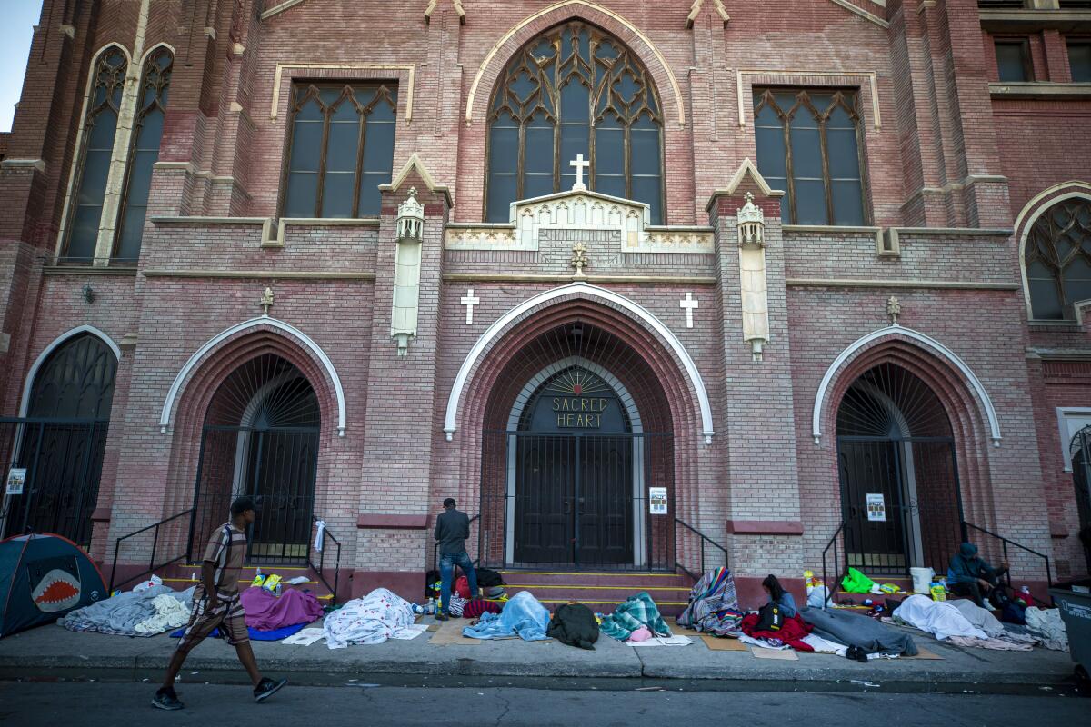 Migrants with bedding wake up at a campsite outside a church.
