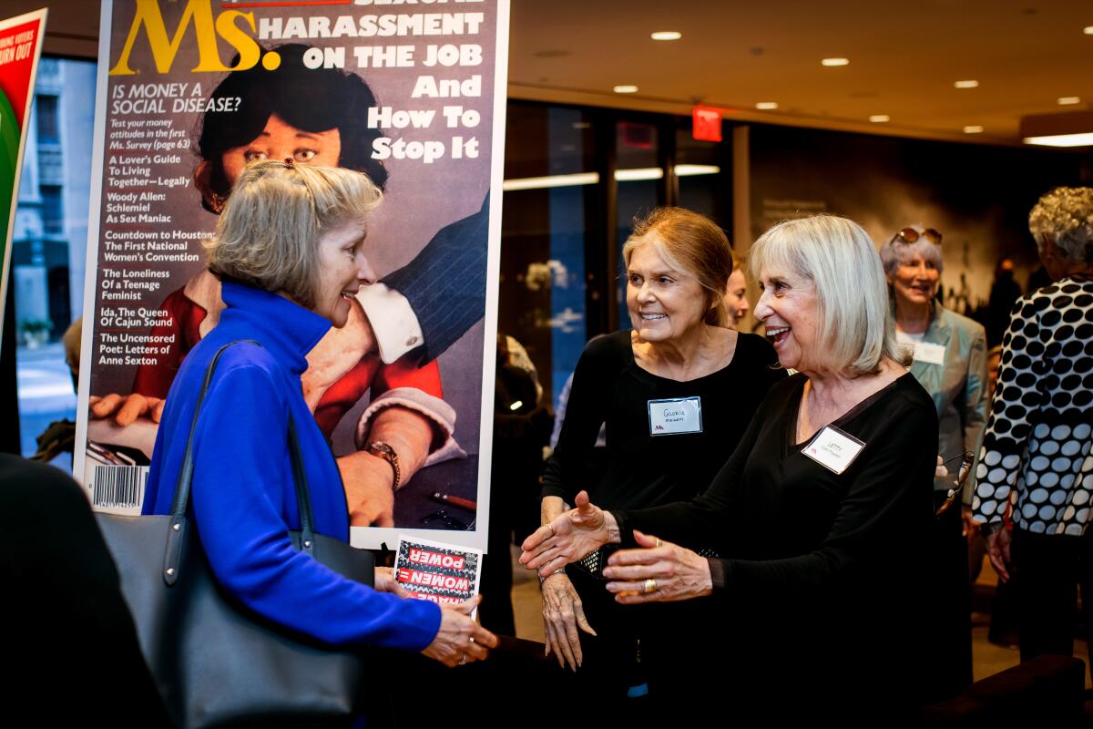 Three older women greet each other at a party.