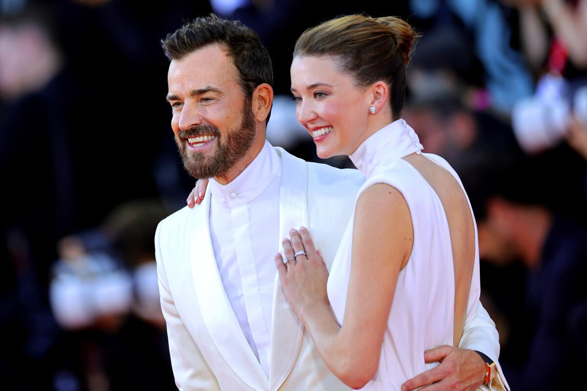 Justin Theroux and Nicole Brydon Bloom posing for photographers wearing all-white with their arms around one another