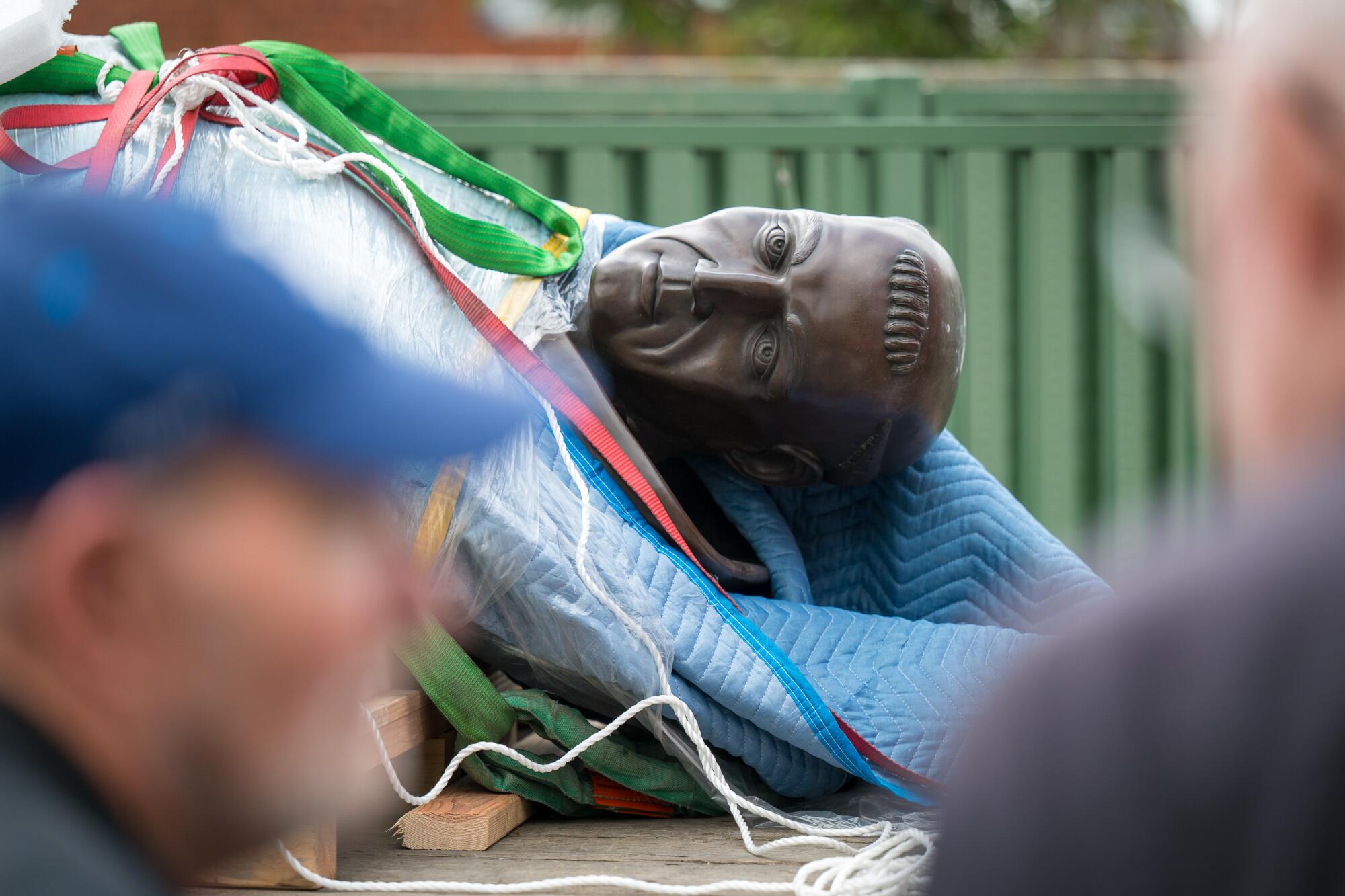 The face of a bronze statue of Junípero Serra emerges from moving blankets and other materials used for its relocation.