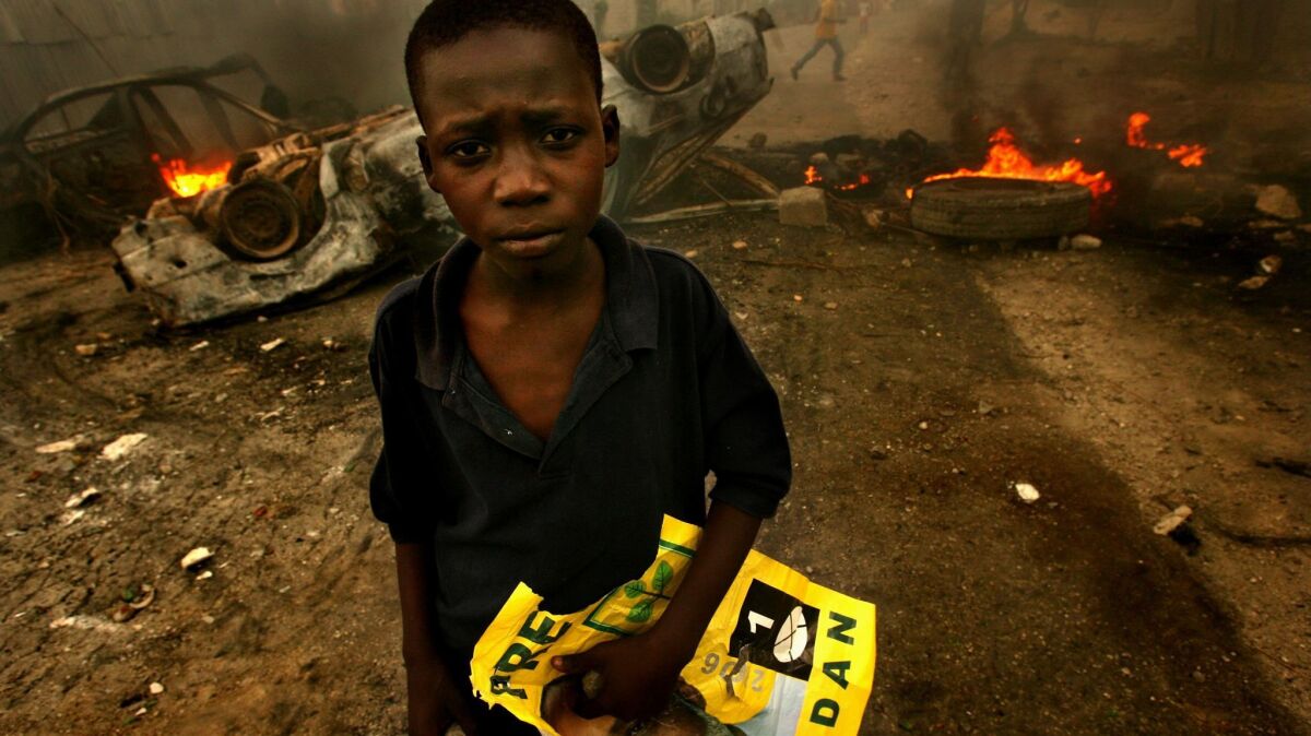 A young Haitian holds a rock and a poster of presidential candidate Rene Preval in front of a burning barricade. Violence broke out after a delay in election results.