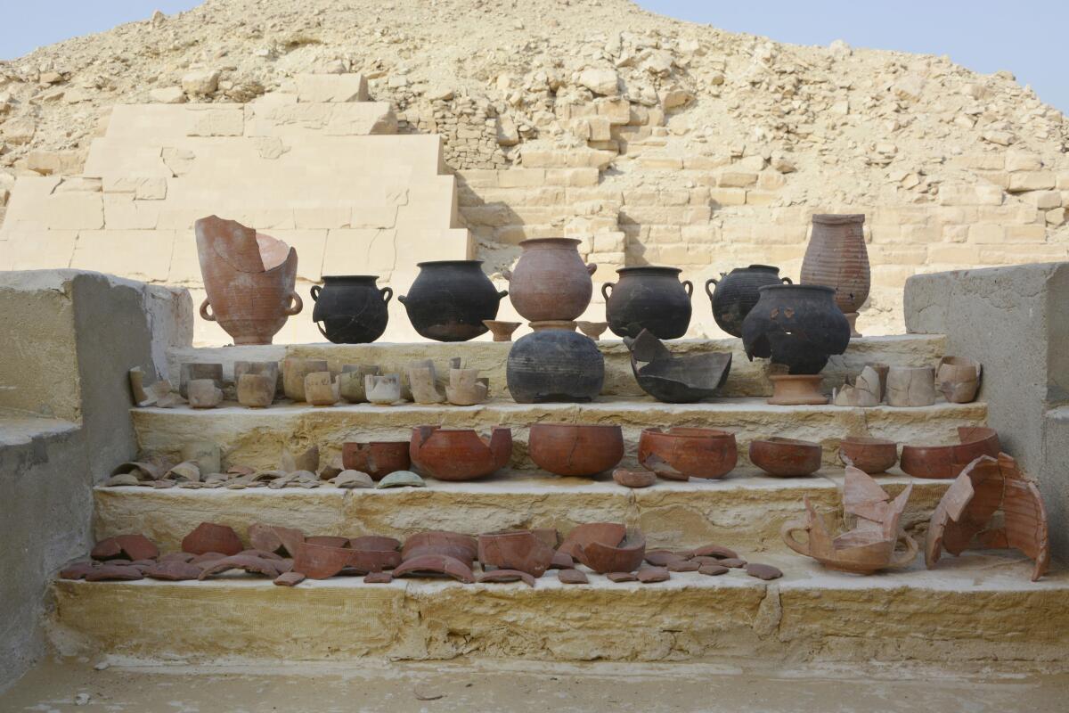 Rows of vessels, some in pieces, sit in front of a ruin. 
