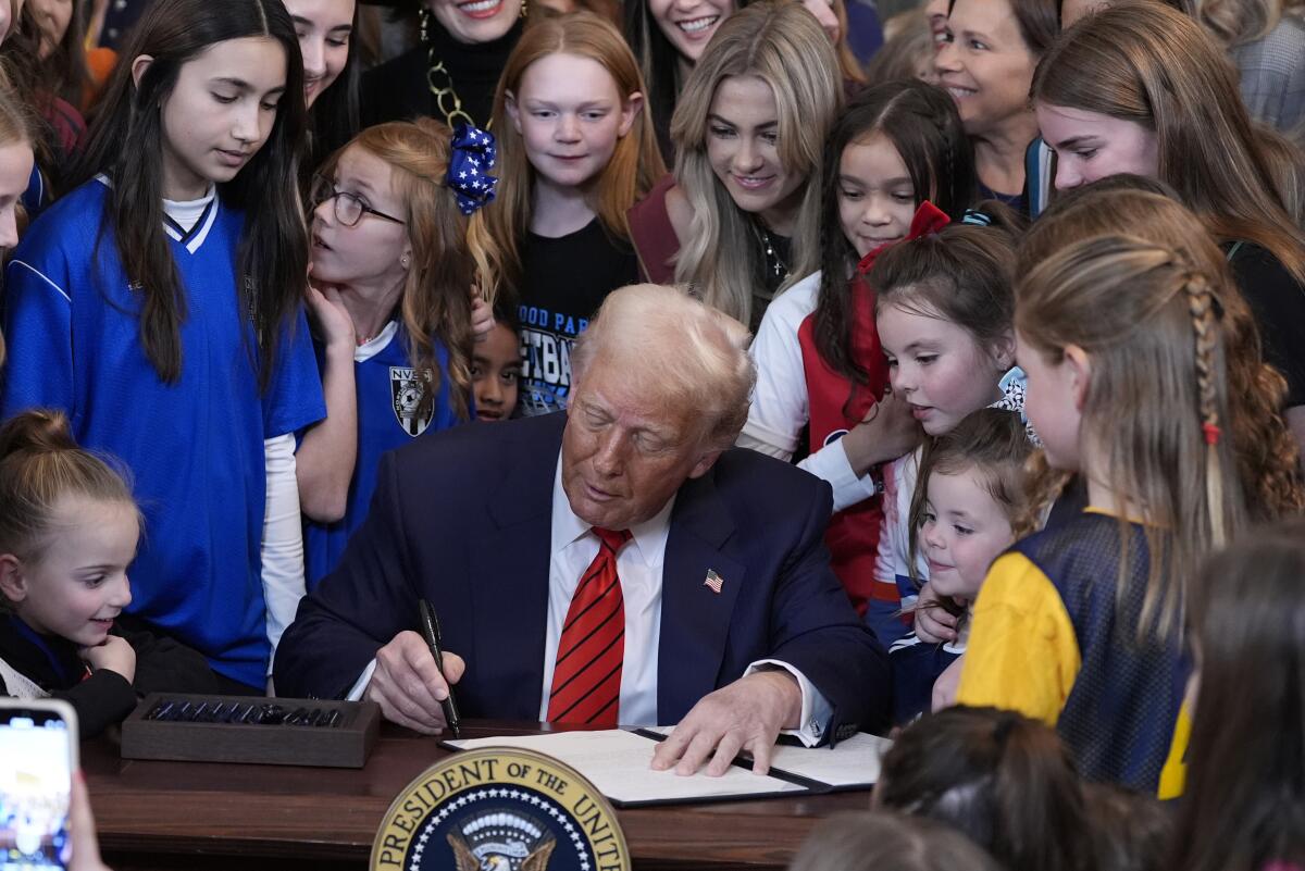 A man signs a paper surrounded by girls