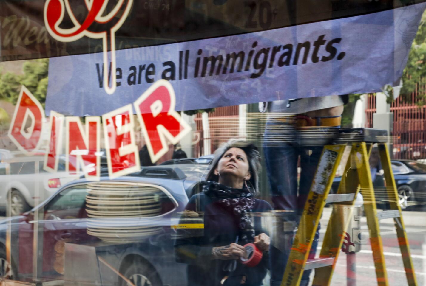 After closing their restaurant for the day, Monica May watches while her partner Kristen Trattner hangs a sign above their Nickel Diner in Downtown Los Angeles in solidarity with a national "Day Without Immigrants."