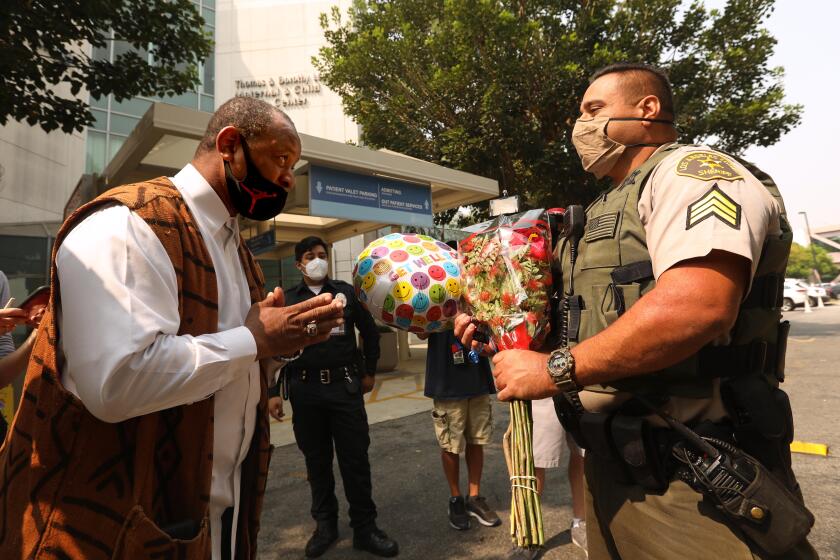 LYNWOOD, CA - SEPTEMBER 14, 2020 - - Najee Ali, director of Project Islamic Hope, raises praying hands after giving Los Angeles Sheriff Sgt. Larry Villareal flowers and a "get well" balloon for the two sheriff deputies who were recovering from being shot in an ambush at the St. Francis Medical Center in Lynwood on September 14, 2020. Two Los Angeles County Sheriff Deputies are in critical condition after being shot in an ambush outside the Compton Metro train station last Saturday night. Ali held a press conference condemning the shooting. "We're here to pray for these officers for a full recovery," Ali said. (Genaro Molina / Los Angeles Times)