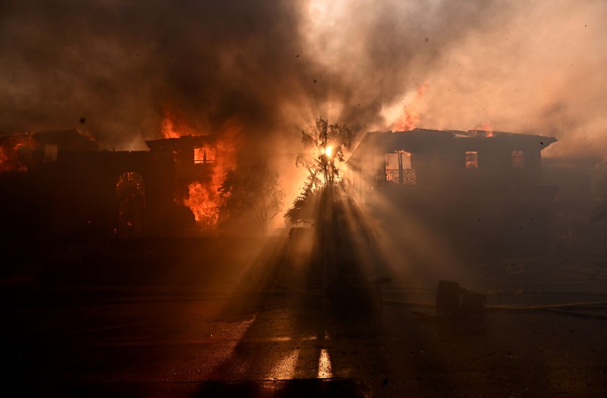 Beams of sunlight shine through the smoke and flames of a burning home in Laguna Niguel.