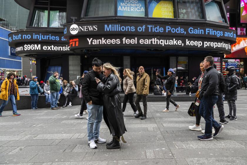 Personas recorren Times Square mientras las pantallas muestran noticias sobre el sismo del viernes 5 de abril de 2024 en Nueva York. (AP Foto/Brittainy Newman)