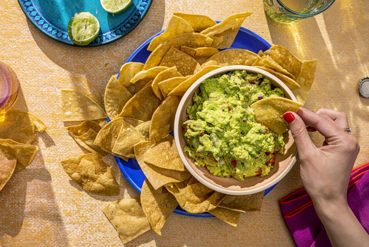 An overhead photo of someone dipping a chip into a bowl of guacamole