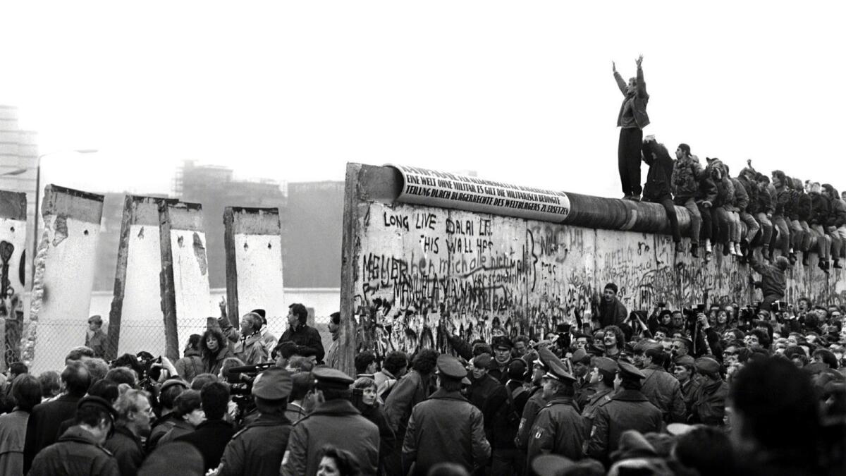 East Germans pour through the Berlin Wall in 1989 as a West Berliner cheers them on from on top.