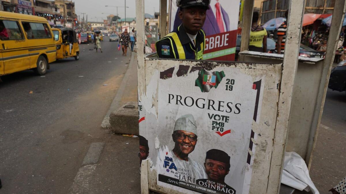 A policeman sits in a roadside post in Lagos, Nigeria, on Dec. 10, 2018, behind a campaign poster of candidates of the ruling All Progressives Congress, Nigerian President Mohammadu Buhari and Vice President Yemi Osinbajo.