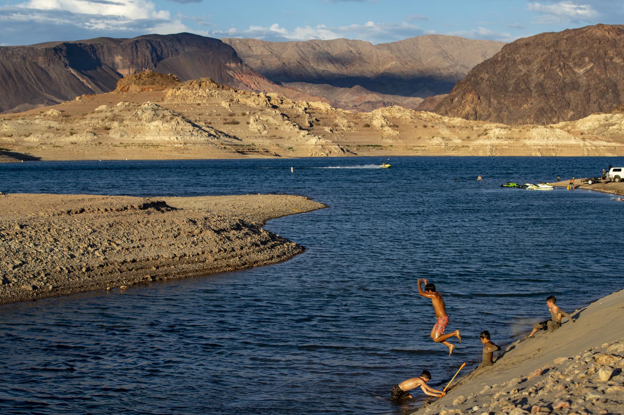 Children cool off jumping into a reservoir surrounded by dry banks and arid mountains. 