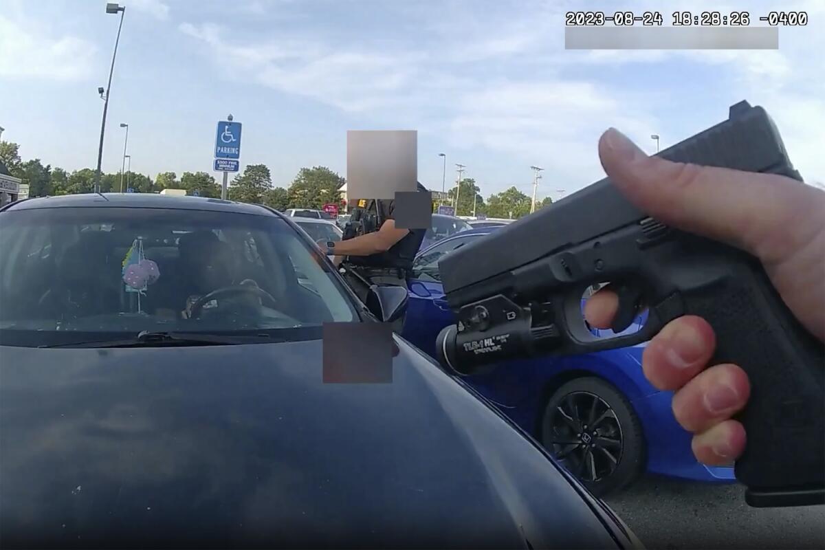 An image from body cam video shows a hand holding a gun pointed toward a windshield as a woman sits in a car.