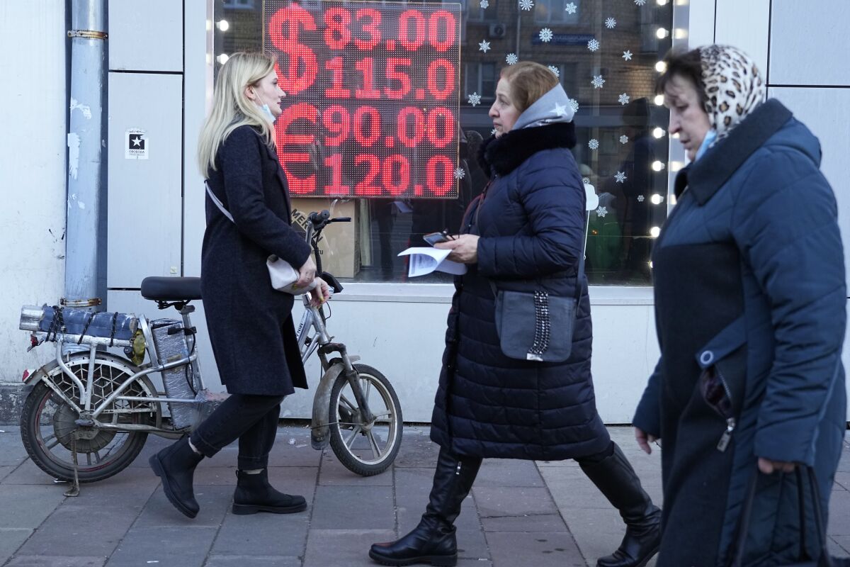 FILE - People walk past a currency exchange office screen displaying the exchange rates of U.S. Dollar and Euro to Russian Rubles in Moscow's downtown, Russia, Feb. 28, 2022. In the days since the West imposed sanctions on Russia over its invasion of Ukraine, ordinary Russians are feeling the painful effects — from payment systems that won't operate and problems withdrawing cash to not being able to purchase certain items. (AP Photo/Pavel Golovkin, File)