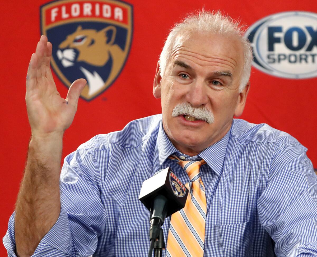 Joel Quenneville sits at a podium and responds to a question during a news conference.