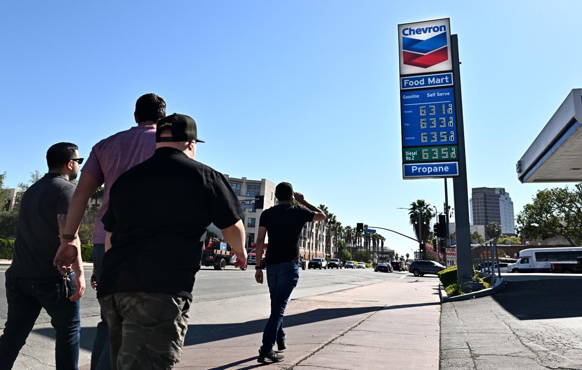 People walk on a sidewalk near a gas station.
