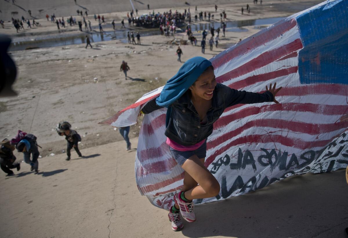 Una migrante carga una bandera estadounidense falsa en la orilla de un río en la frontera de México con Estados Unidos después de que varios de ellos rebasaran a la policía mexicana en el cruce fronterizo de Chaparral en Tijuana, México.