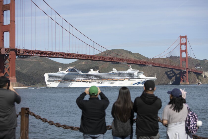 Five people, some with binoculars, look at a cruise ship as it sails under the Golden Gate Bridge 