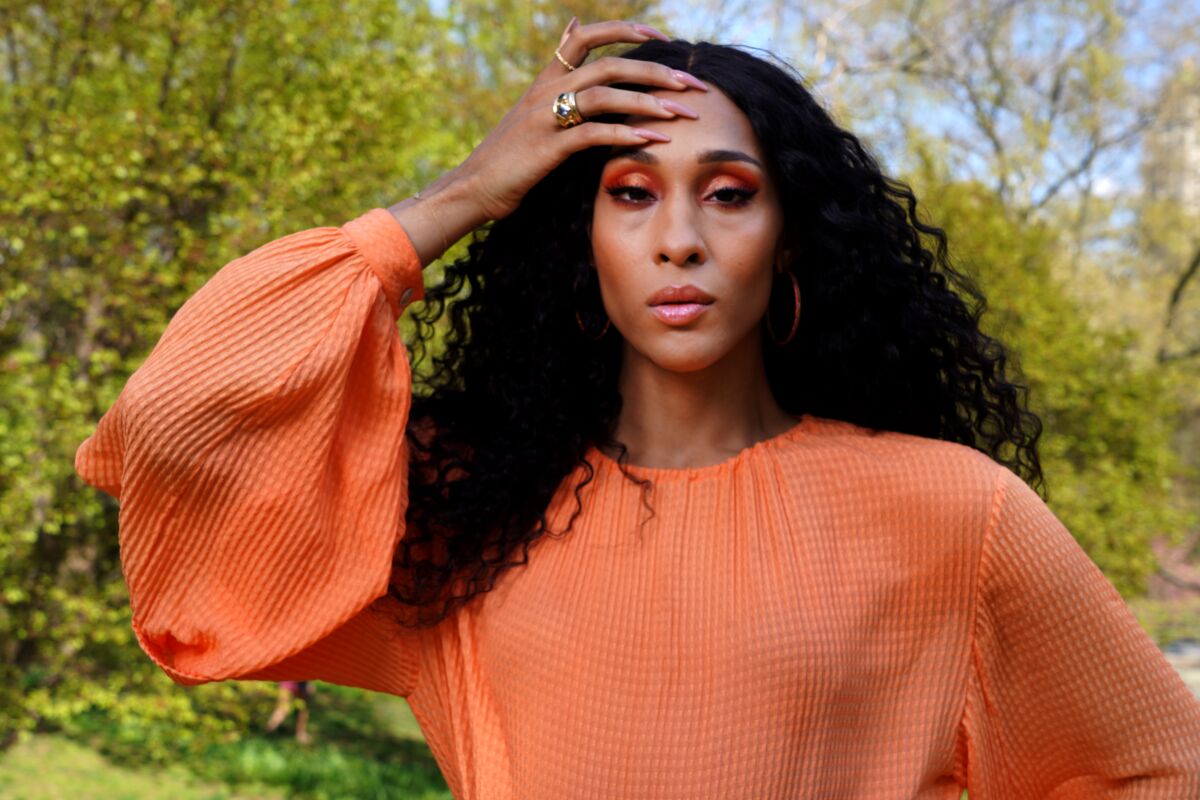 'Pose' actor Mj Rodriguez in an orange top with her hand on her head, pictured outdoors