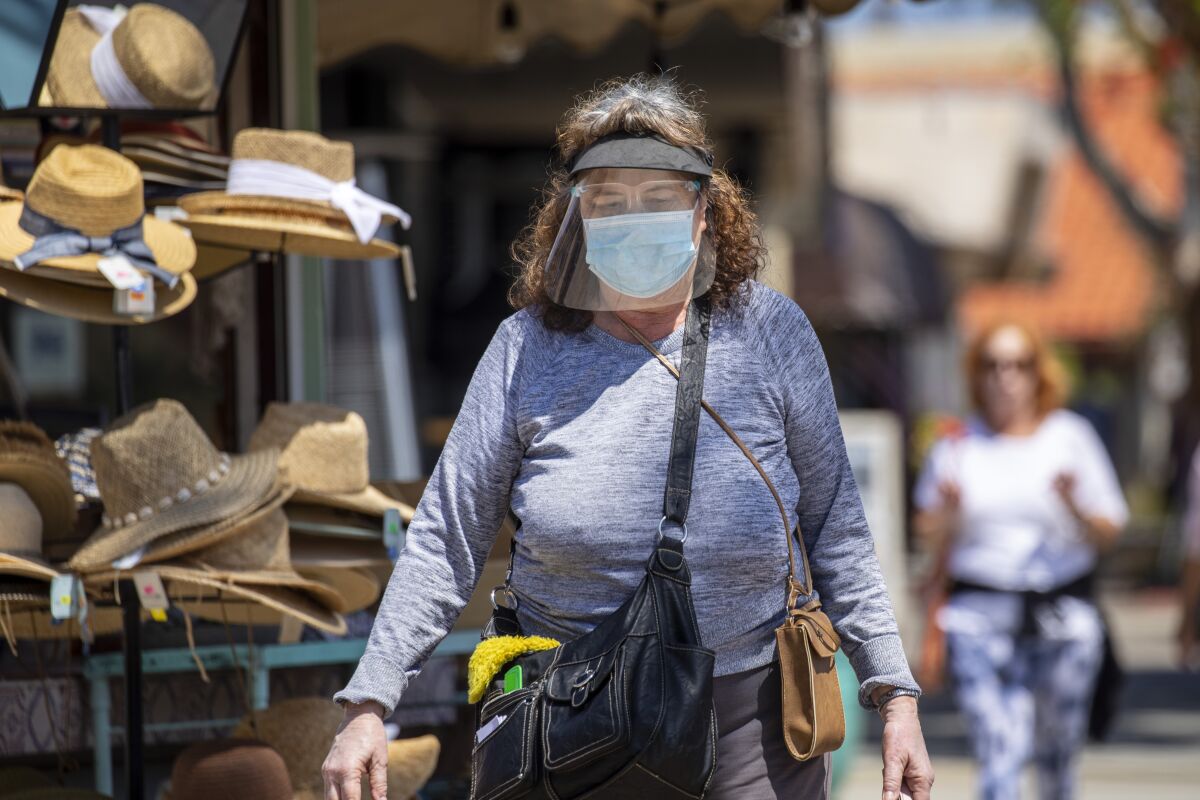 A woman in a mask and face shield walks 