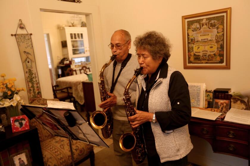 REDLANDS, CA - NOVEMBER 30, 2023 - Danny Perez, 81, left, and his wife Martha Perez, 83, play a religious song on saxophone in their home in Redlands on November 30, 2023. The Perez' are members of the Seventh Day Adventist Church and practice the lifestyle of seniors who live in the Blue Zone in the nearby town of Loma Linda. The Perez' believe that faith, diet and an active lifestyle has contributed to a longer life. A recent Netflix mini series, "Live to 100: Secrets of the Blue Zones," claims Loma Lindan's live longer due to faith, diet, and exercise. Blue zones are regions in the world where people are claimed to live, or to have recently lived, longer than average. The notion is not based on scientific evidence but demographic anecdotes. (Genaro Molina / Los Angeles Times)