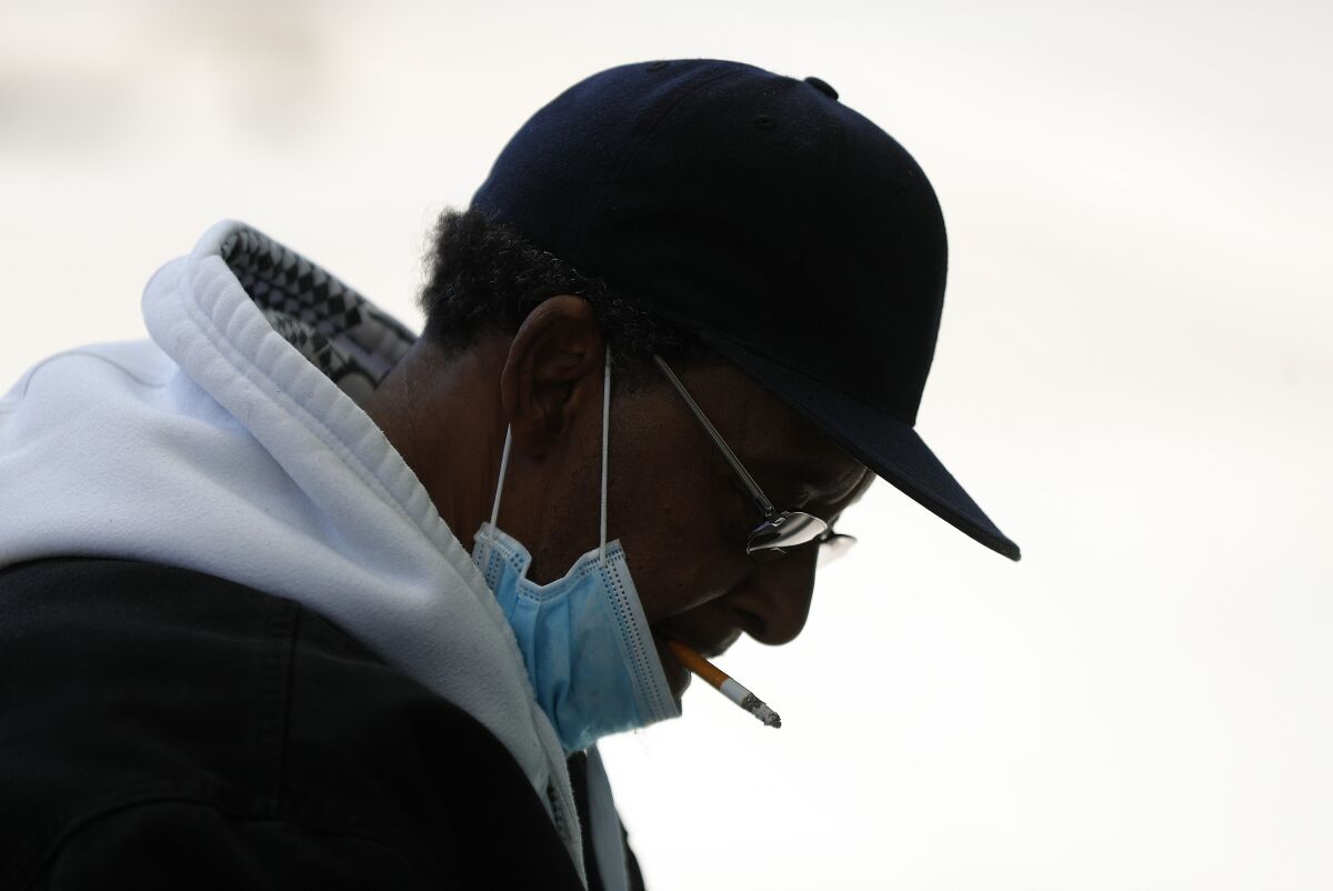FILE - A man with a protective mask smokes a cigarette while waiting for a bus in Detroit, Wednesday, April 8, 2020. U.S. cigarette smoking dropped to a new all-time low in 2020, with 1 in 8 adults saying they were current smokers, according to survey data released Thursday, March 17, 2022, by the Centers for Disease Control and Prevention. Adult e-cigarette use also dropped, the CDC reported. (AP Photo/Paul Sancya, File)