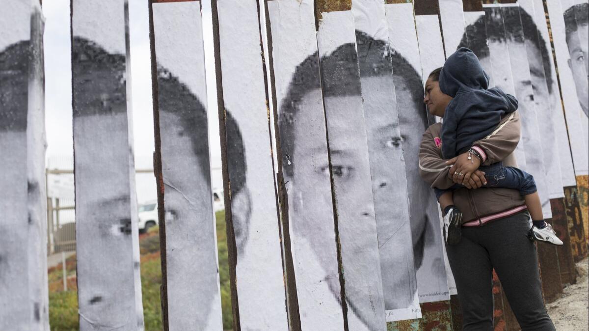 A Central American migrant, holding a child, looks through the border wall with the U.S. in Tijuana, Mexico on April 29. U.S. immigration lawyers are telling a caravan of asylum-seekers that they face possible separation from their children and detention for many months.