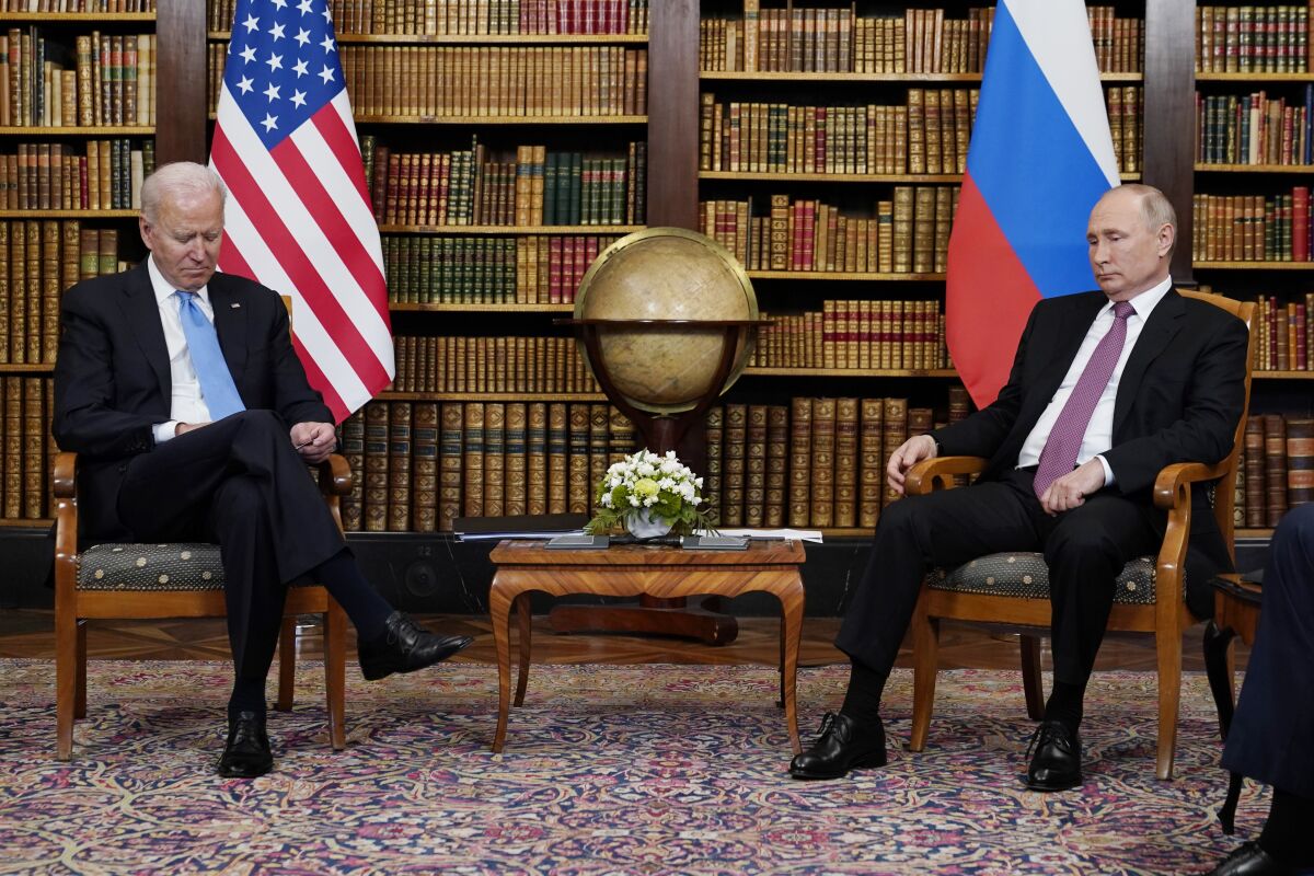 President Biden and Russian President Vladimir Putin sit in front of flags and shelves of books 