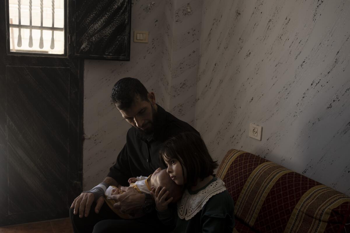 A Palestinian man holds an infant as he sits by a 5-year-old girl. 