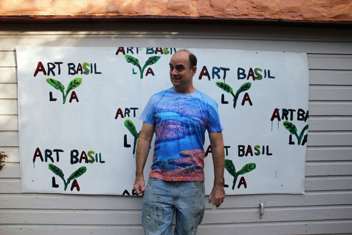"Art Basil" mastermind John Kilduff stands in front of his handmade step-and-repeat logo billboard — painted on cardboard.